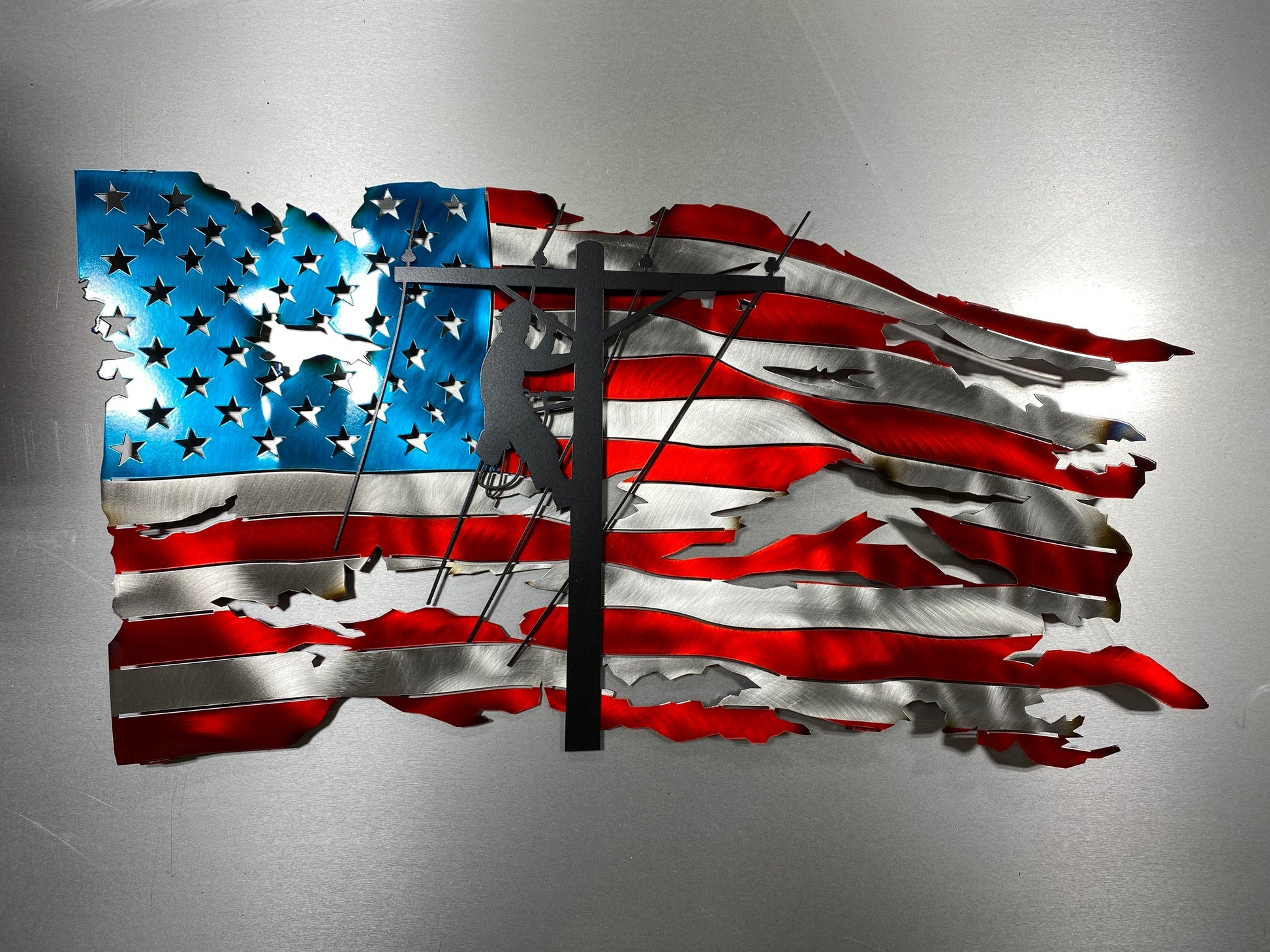 Handcrafted metal American flag with lineman silhouette in powder-coated candy red, blue, and black. Built for indoor or outdoor display.