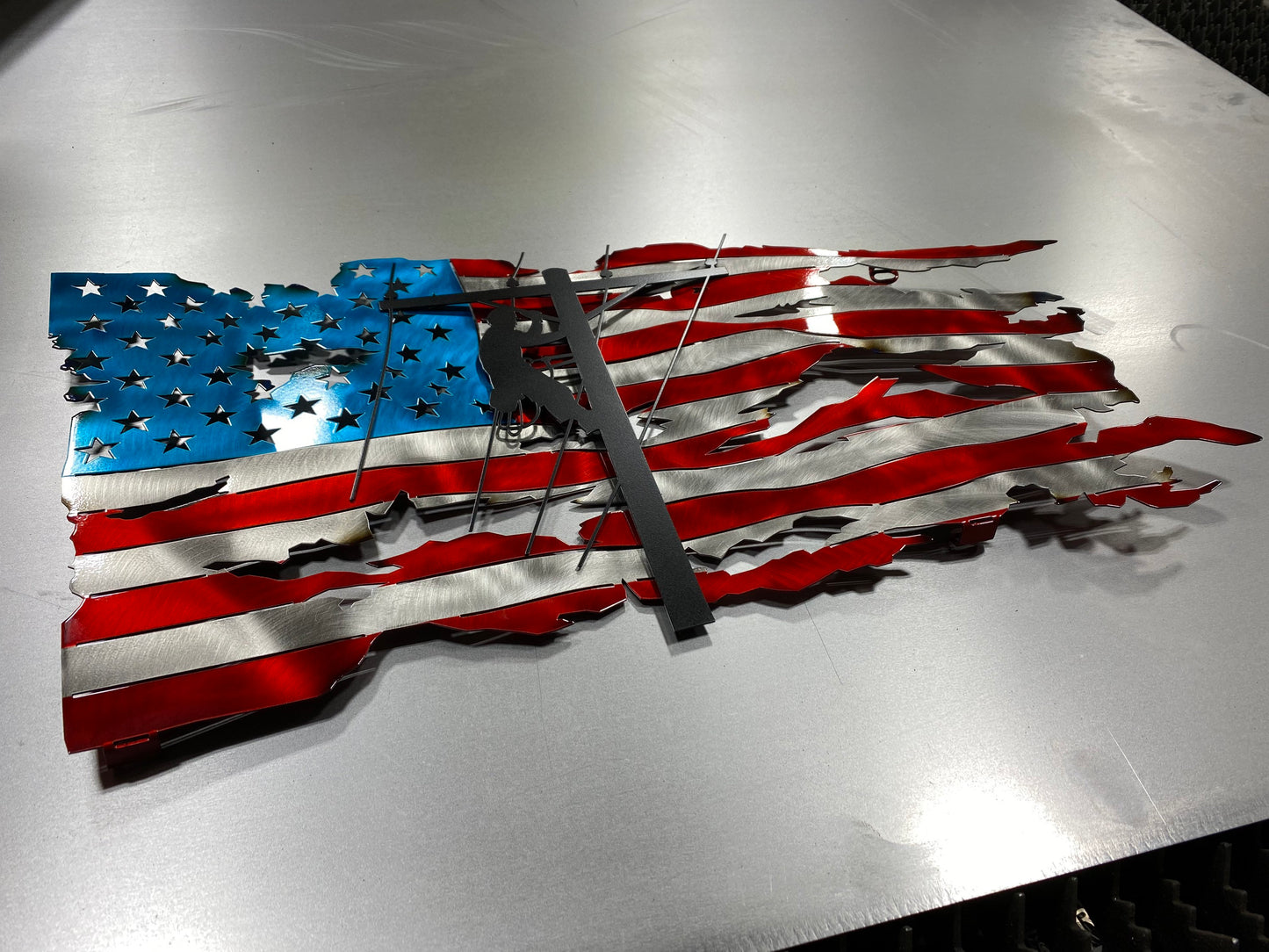 Handcrafted metal American flag with lineman silhouette in powder-coated candy red, blue, and black. Built for indoor or outdoor display.