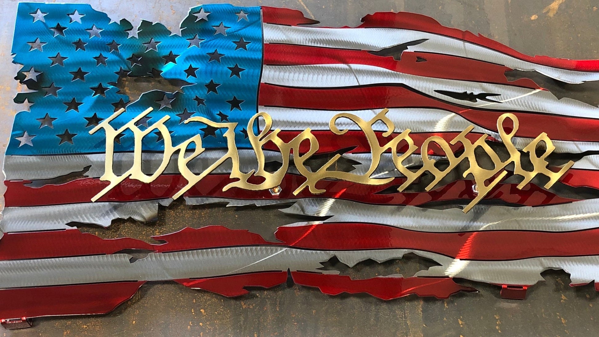 We The People Battle Worn Metal Flag, handcrafted from American steel with a rugged, battle-worn design and powder-coated finish