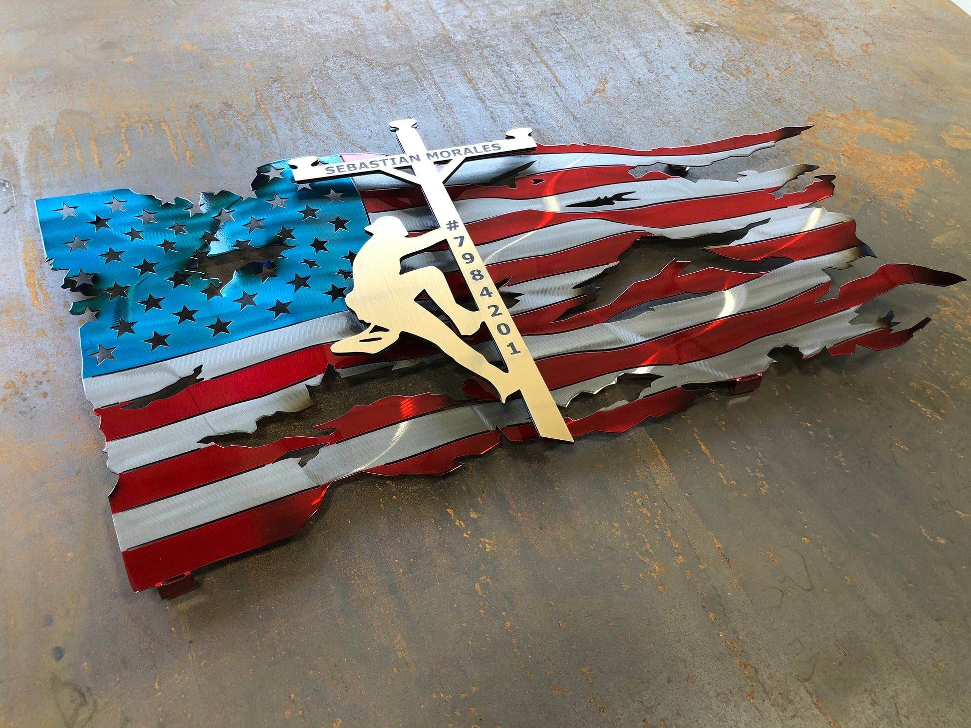 Lineman American Flag featuring a wavy battle-worn metal design with a customizable floating gold lineman. Engraved details available.