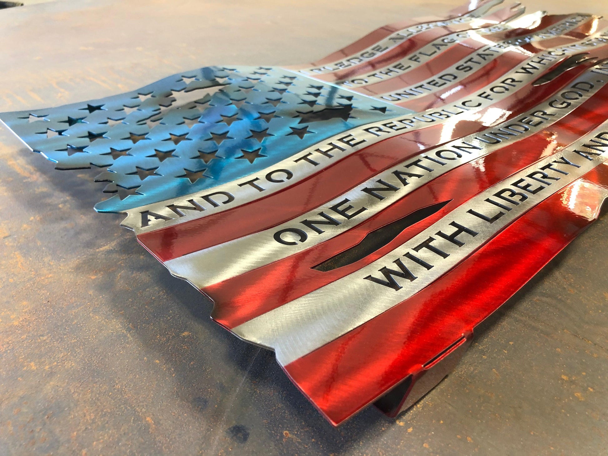 Pledge of Allegiance metal flag with hand-formed waves, heat patina finish, and floating wall mount design, measuring 24 inches wide.