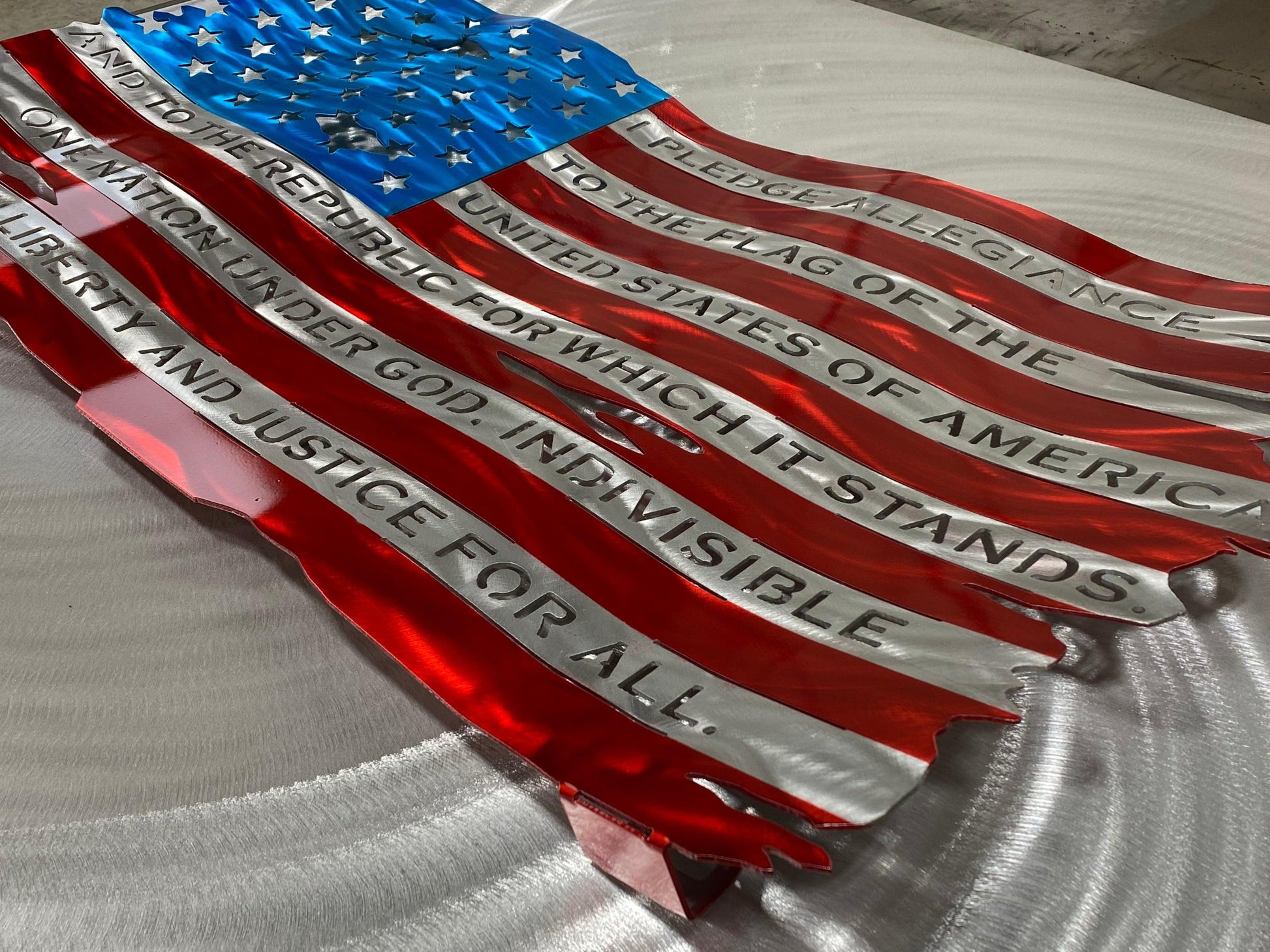 Pledge of Allegiance metal flag with hand-formed waves, heat patina finish, and floating wall mount design, measuring 24 inches wide.