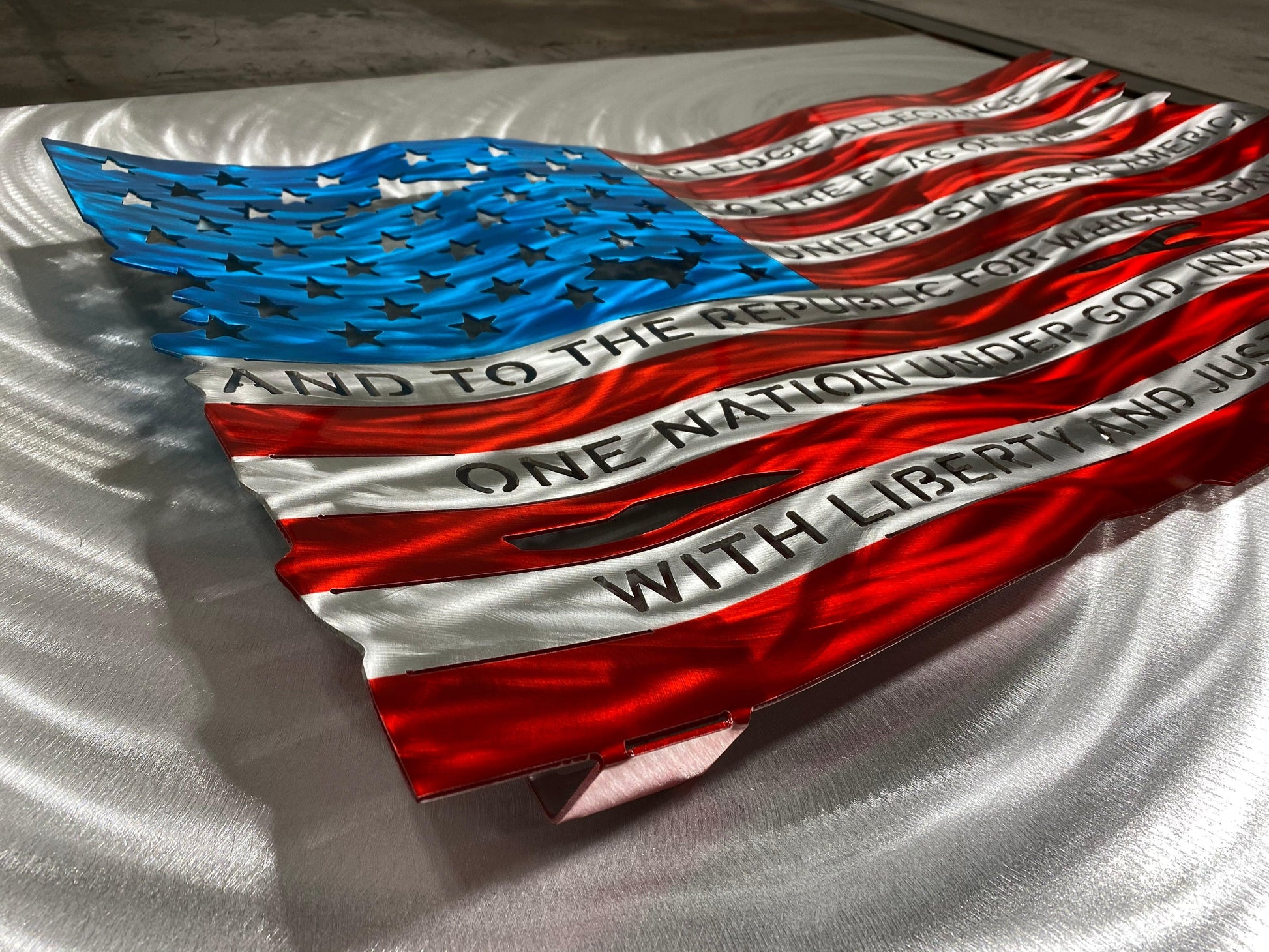 Pledge of Allegiance metal flag with hand-formed waves, heat patina finish, and floating wall mount design, measuring 24 inches wide.