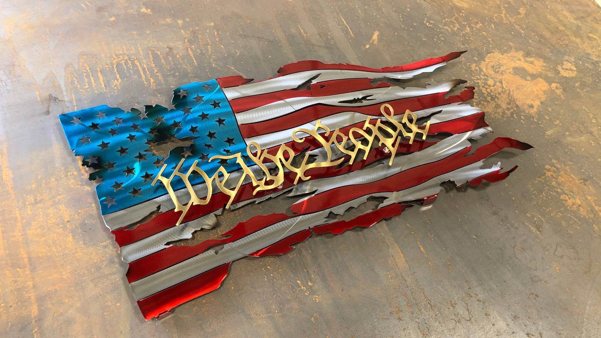 We The People Battle Worn Metal Flag, handcrafted from American steel with a rugged, battle-worn design and powder-coated finish