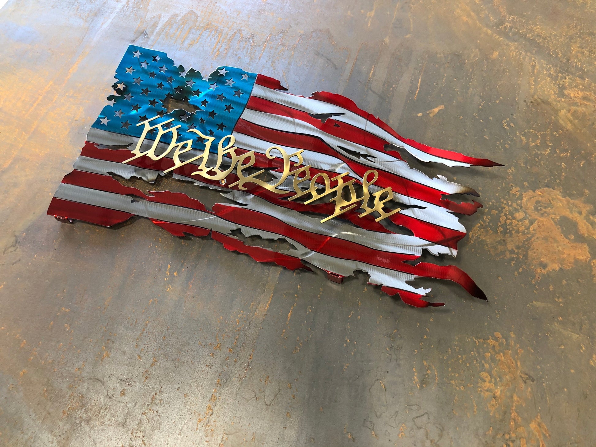 We The People Battle Worn Metal Flag, handcrafted from American steel with a rugged, battle-worn design and powder-coated finish