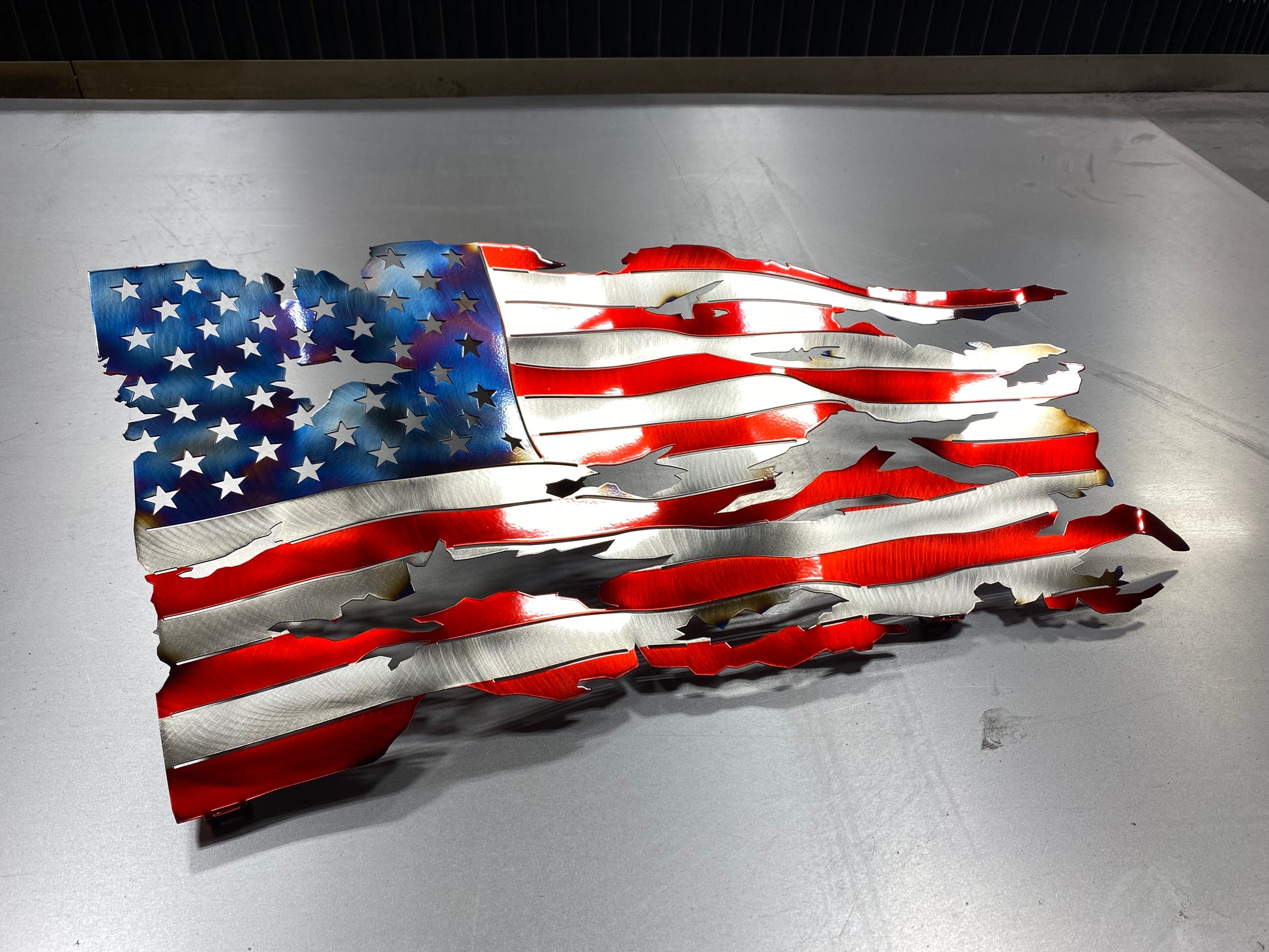 Battle-worn waving metal American flag with heat patina accents, handcrafted and powder-coated in Candy Red for indoor and outdoor display by CnS CnC.