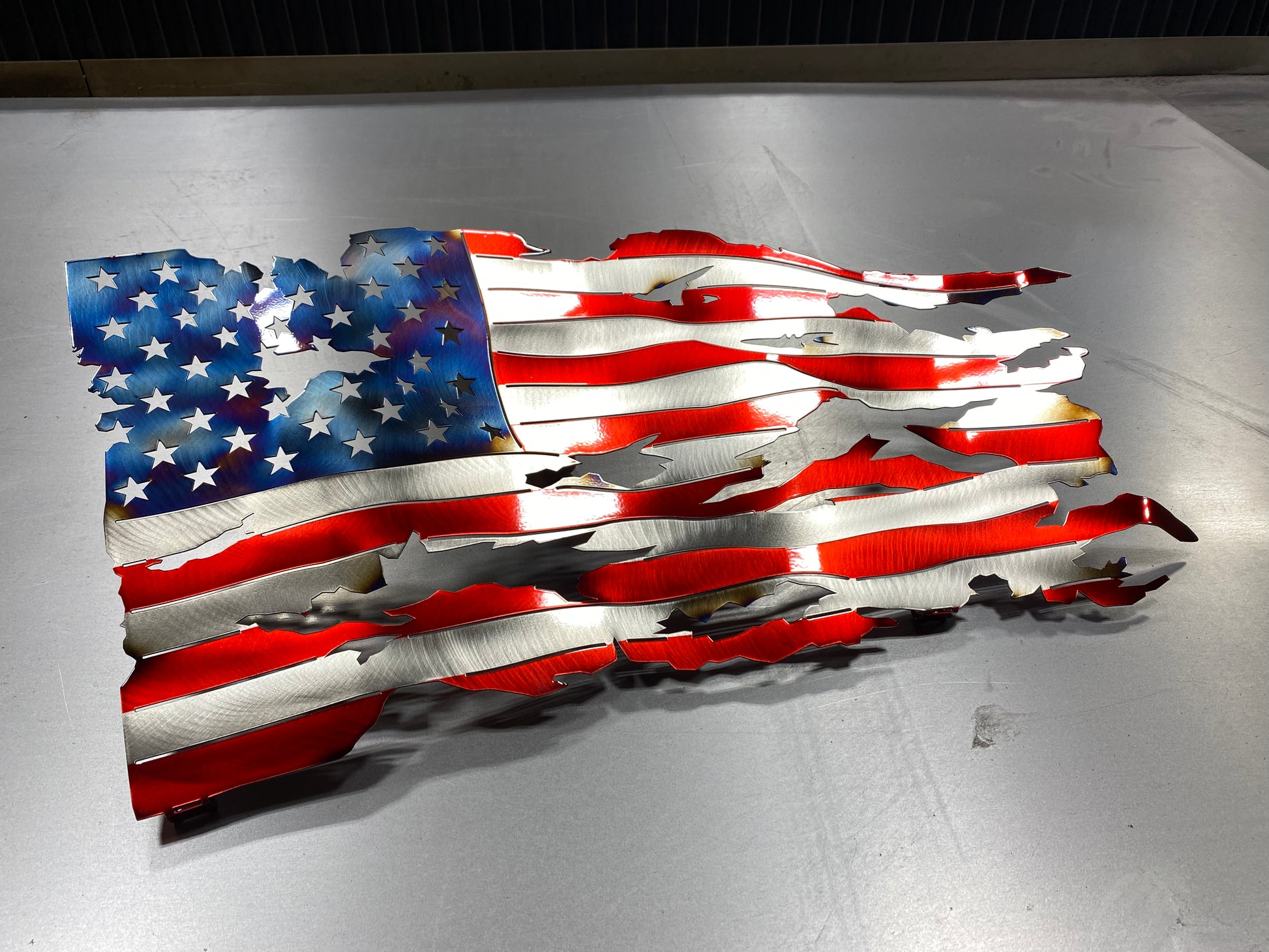 Battle-worn waving metal American flag with heat patina accents, handcrafted and powder-coated in Candy Red for indoor and outdoor display by CnS CnC