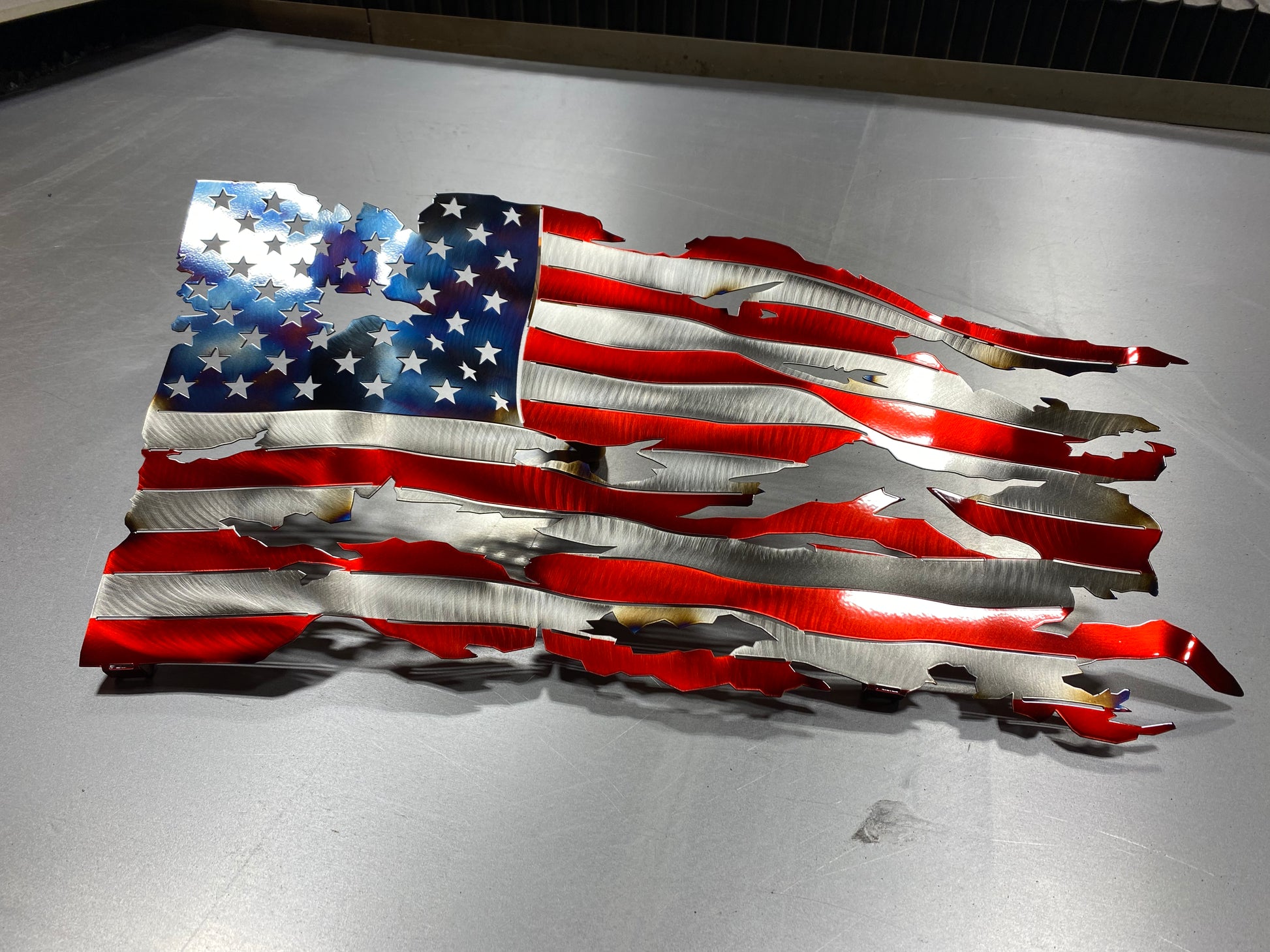 Battle-worn waving metal American flag with heat patina accents, handcrafted and powder-coated in Candy Red for indoor and outdoor display by CnS CnC.